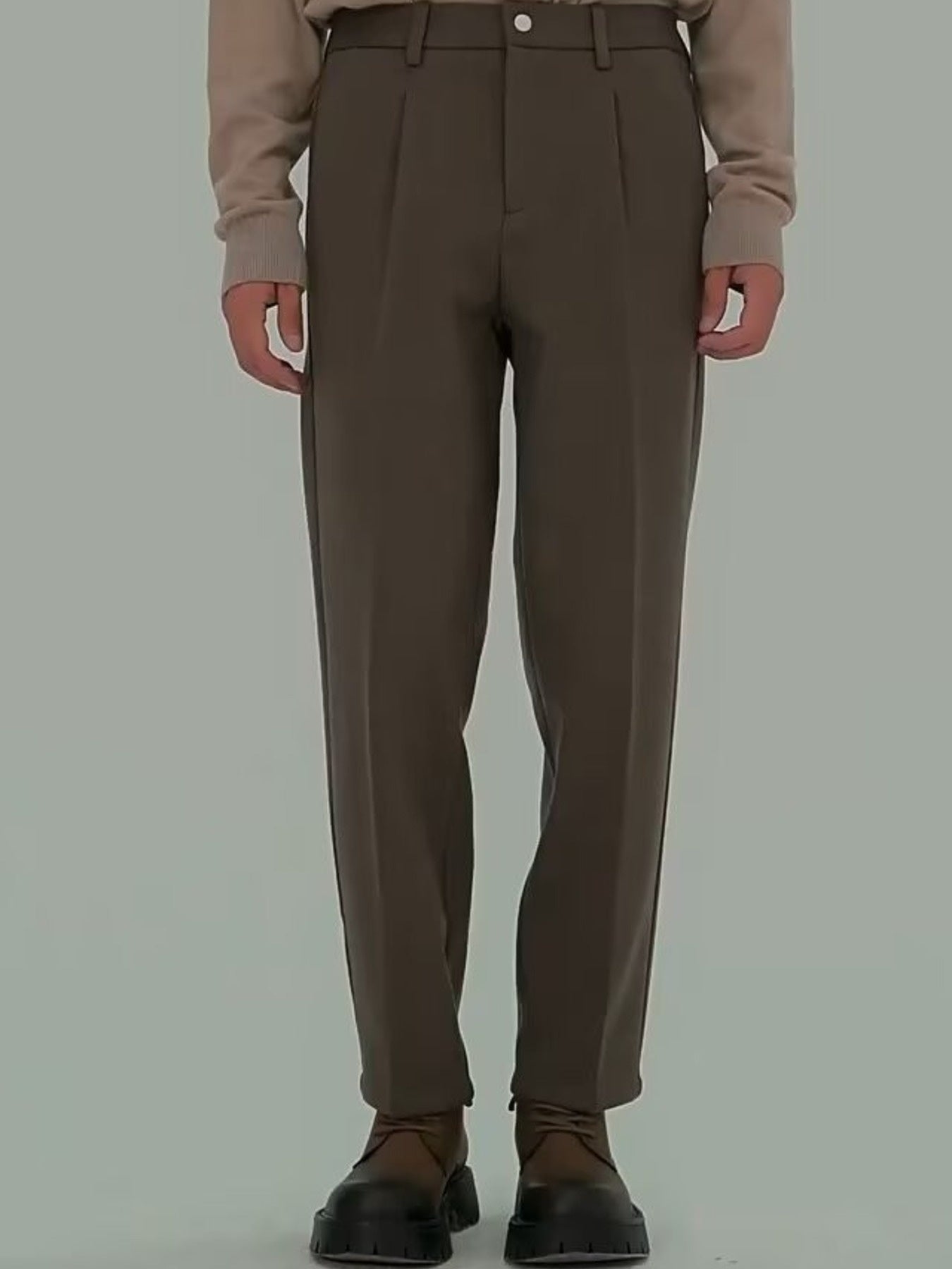 Men's brown pleated trousers with a relaxed fit and visible pockets.