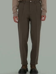 Men's brown pleated trousers with a relaxed fit and visible pockets.