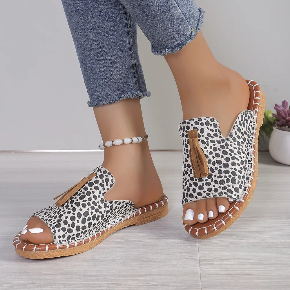 Spotted tassel slide sandals in ivory with a brown sole and stitching.