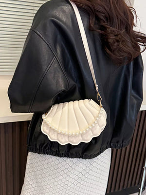 White shell crossbody bag with pearl trim, worn with a black jacket.