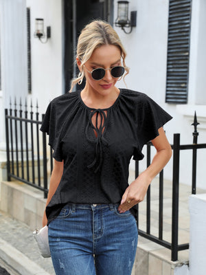Black perforated tie-neck blouse with flutter sleeves and a diamond pattern.