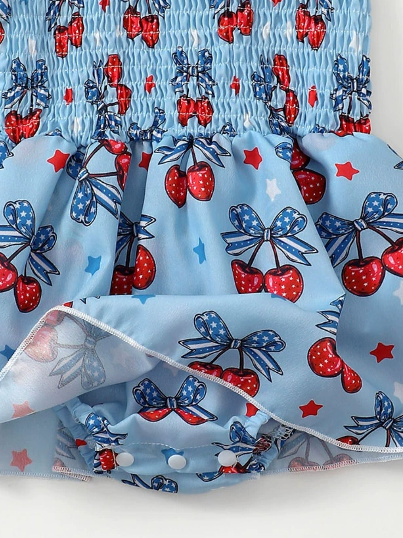 Baby bodysuit dress with cherry and bow print, smocked bodice, and snap closure.