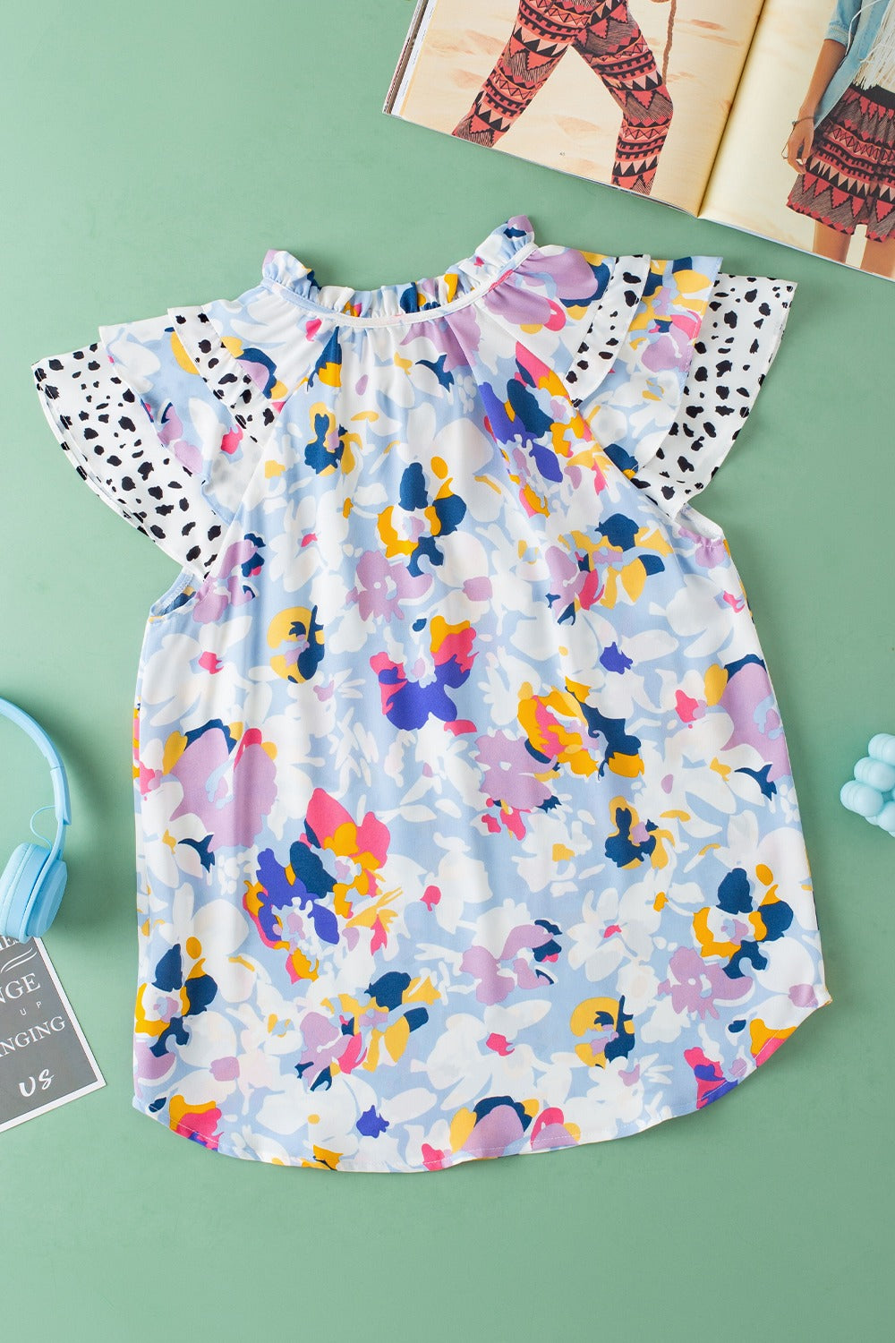 Dalmatian Trim Floral Print Blouse in light blue with ruffled neckline and flutter sleeves.