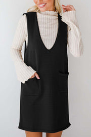 Black V-neck sleeveless sweater dress with pockets, styled over a cream ribbed turtleneck.