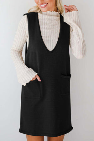 Black V-neck sleeveless sweater dress with pockets, styled over a cream ribbed turtleneck.