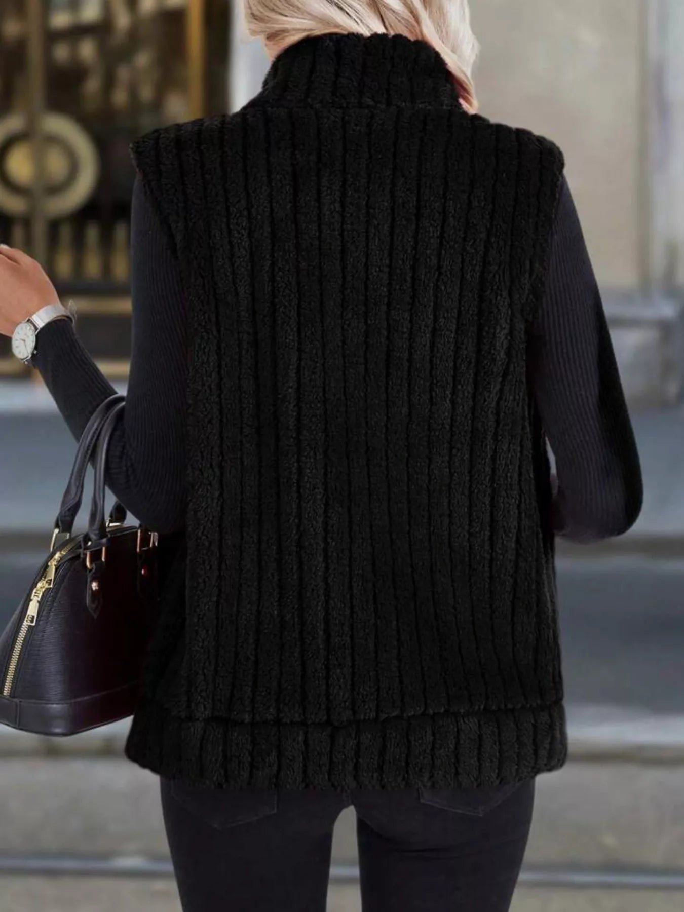 Black fleece zip-up vest with vertical ribbing and a mock neck, layered over a black sweater.