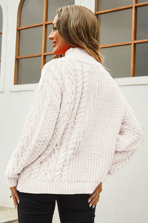 Beige cable-knit turtleneck sweater with voluminous silhouette and textured details.
