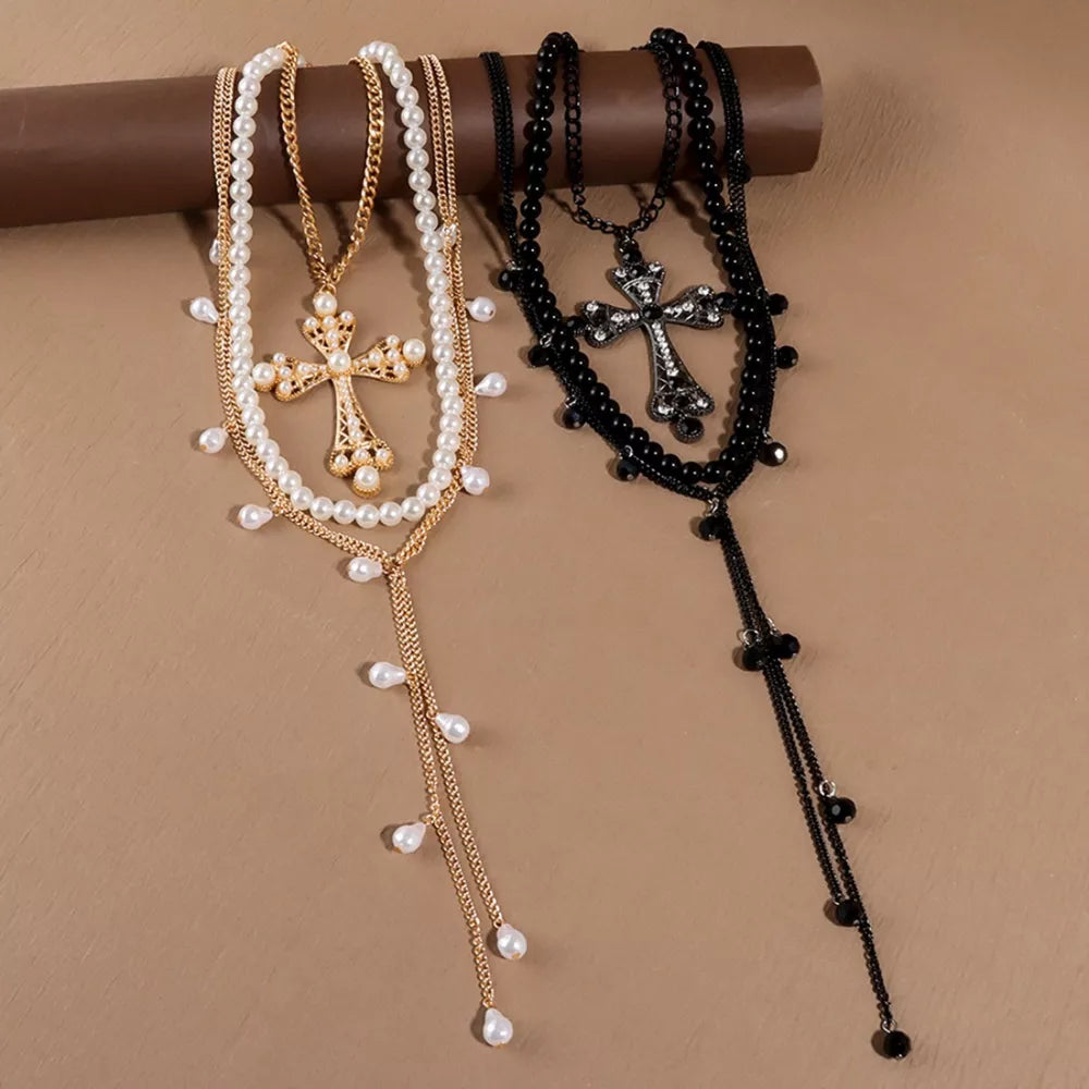 Gold and black pearl cross pendant necklaces with layered chains and dangling pearls.