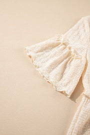 Beige textured blouse with ruffled short sleeves and hemline detail.