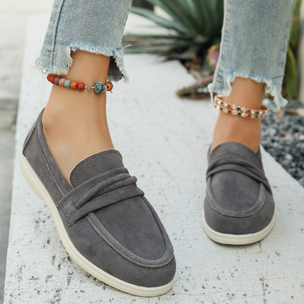 Grey slip-on loafers with ruched strap detail and white soles.