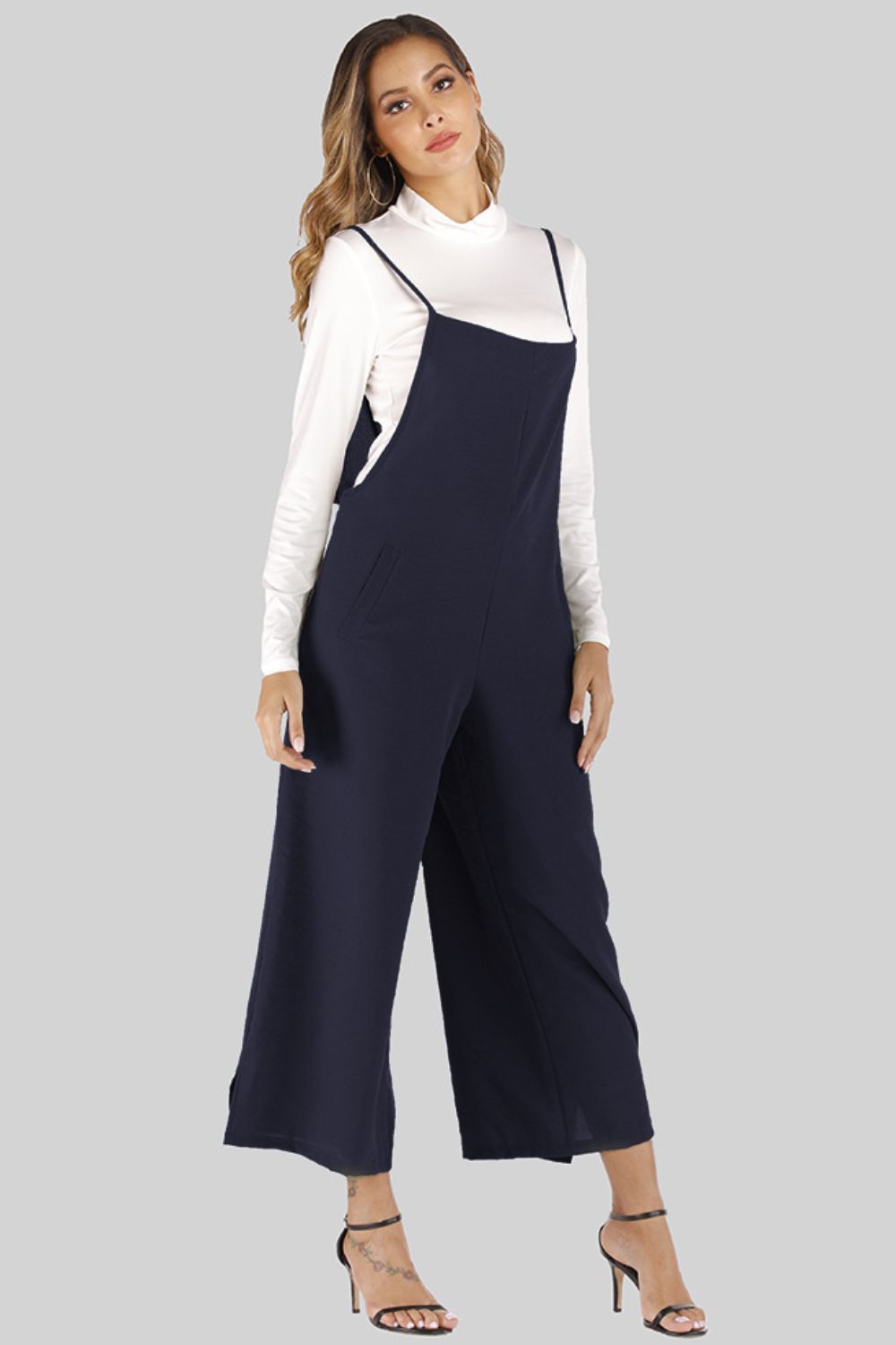 Dark navy culotte overalls with slender straps and wide legs, worn over a white turtleneck.