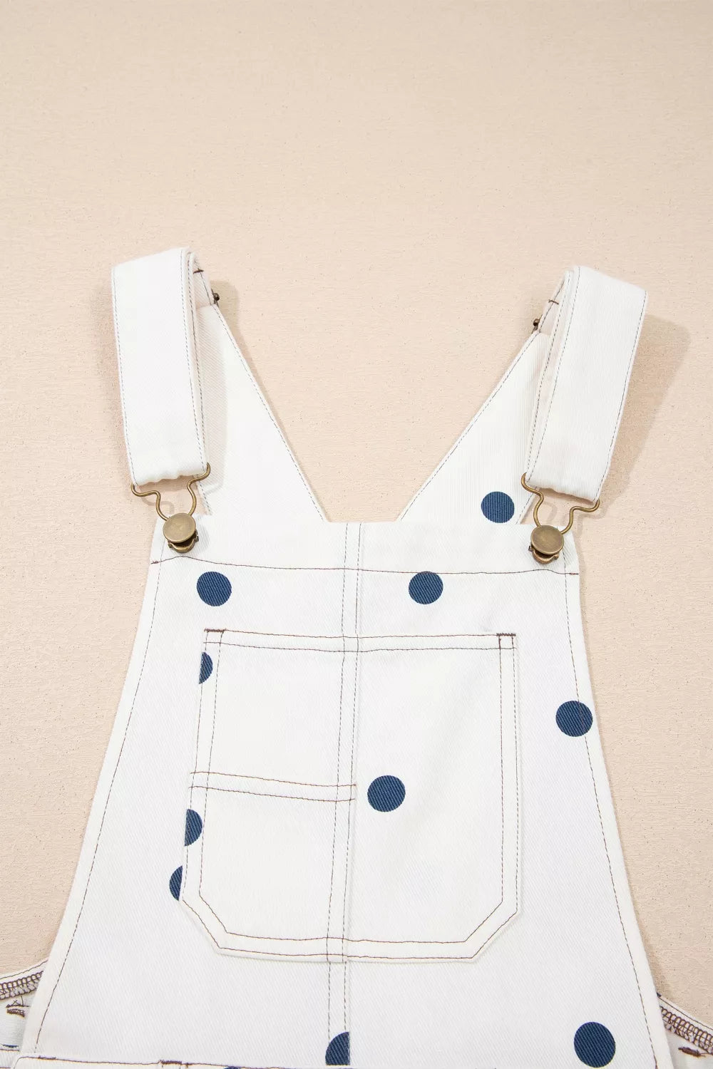 White denim overalls with navy polka dots and adjustable straps.