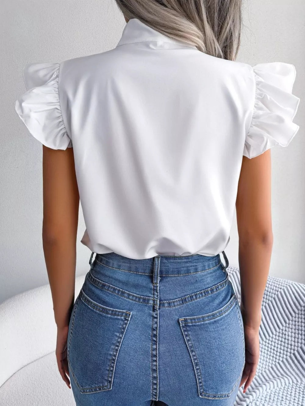 White pussy-bow blouse with ruffled cap sleeves, shown from the back.