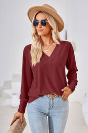 Burgundy textured V-neck blouse with button cuff detail and long sleeves.