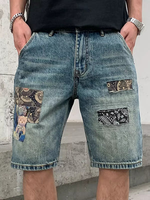 Men's blue denim shorts with graphic patchwork details and a distressed finish.