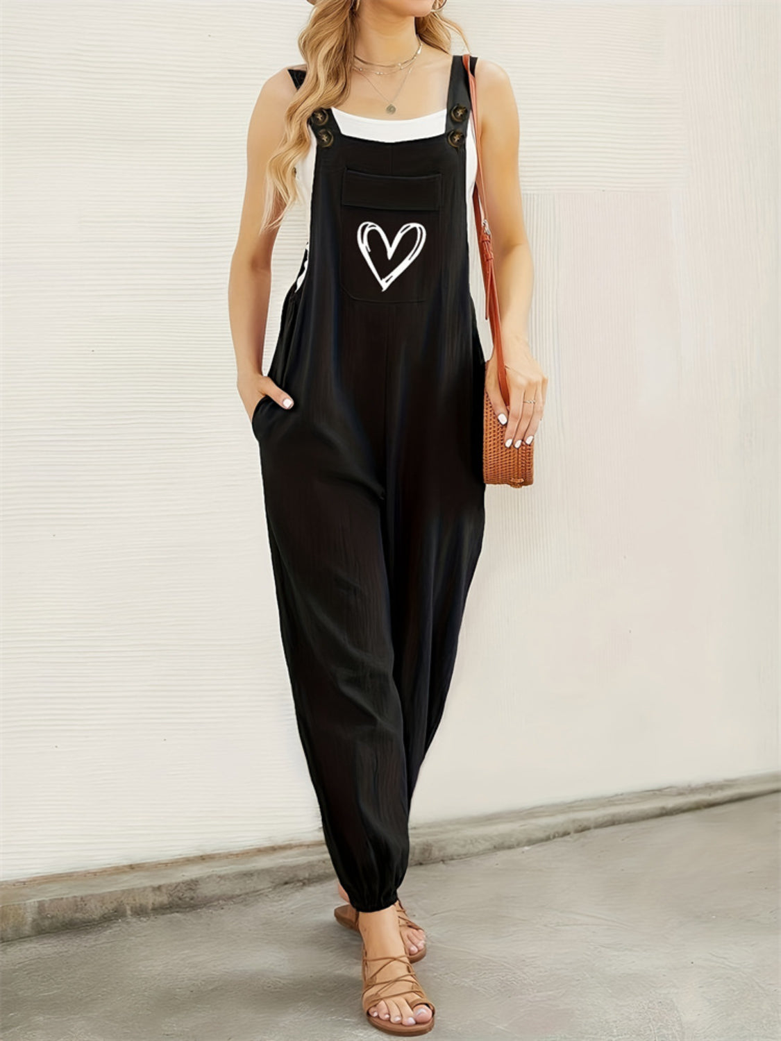 Black cotton overalls jumpsuit with white heart pocket detail, wide leg, and adjustable straps.