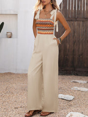Smocked tie shoulder romper in beige with a patterned bodice and wide legs.