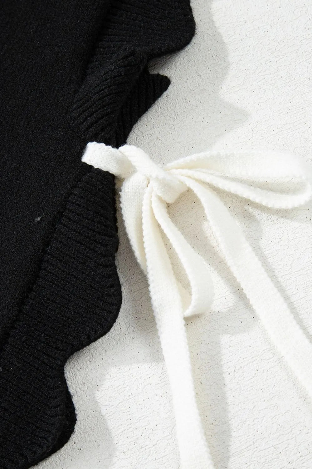 Black knit vest with scalloped hem and white bow detail