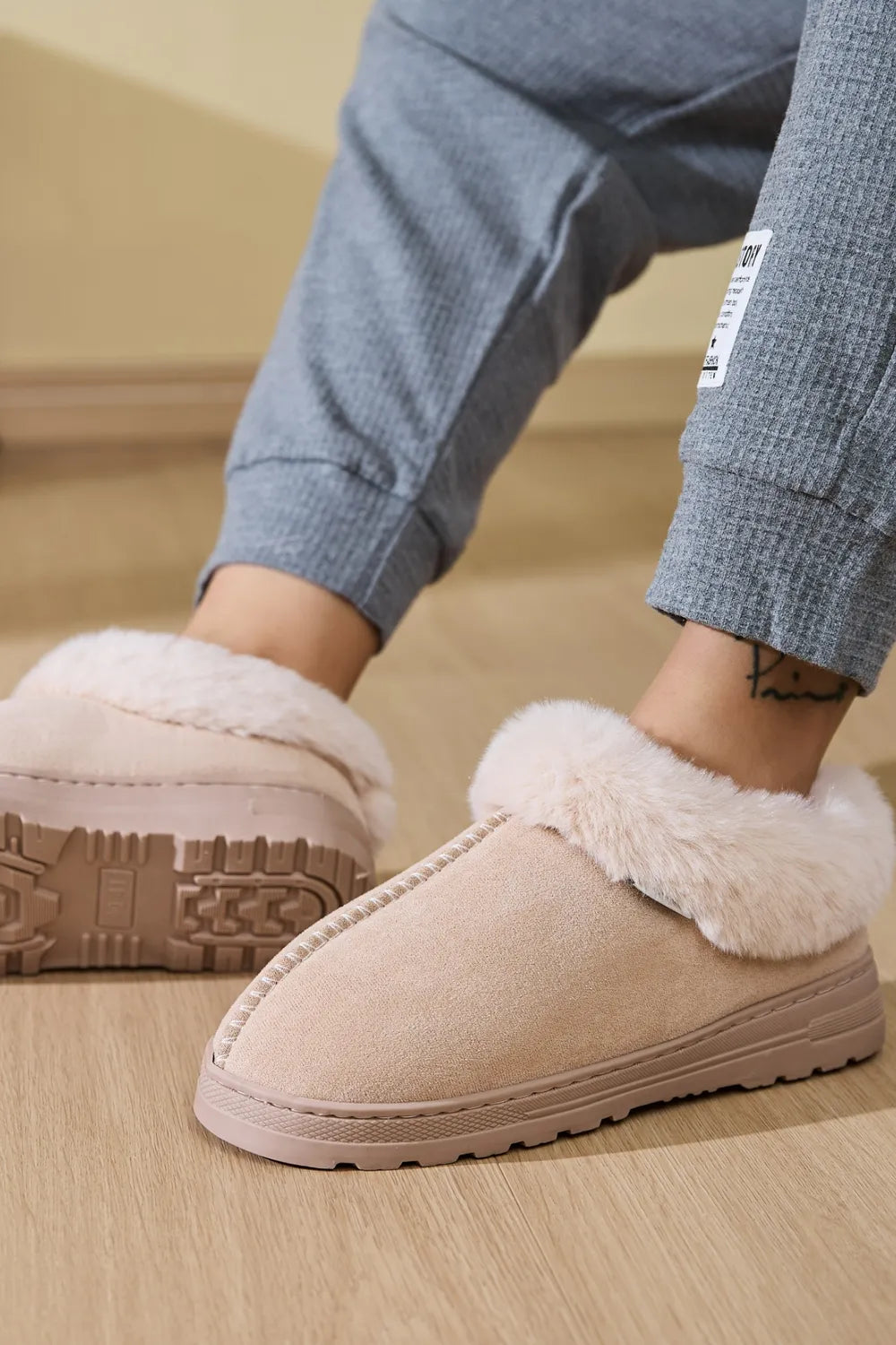 Suede house slippers with plush shearling trim in a light beige color.