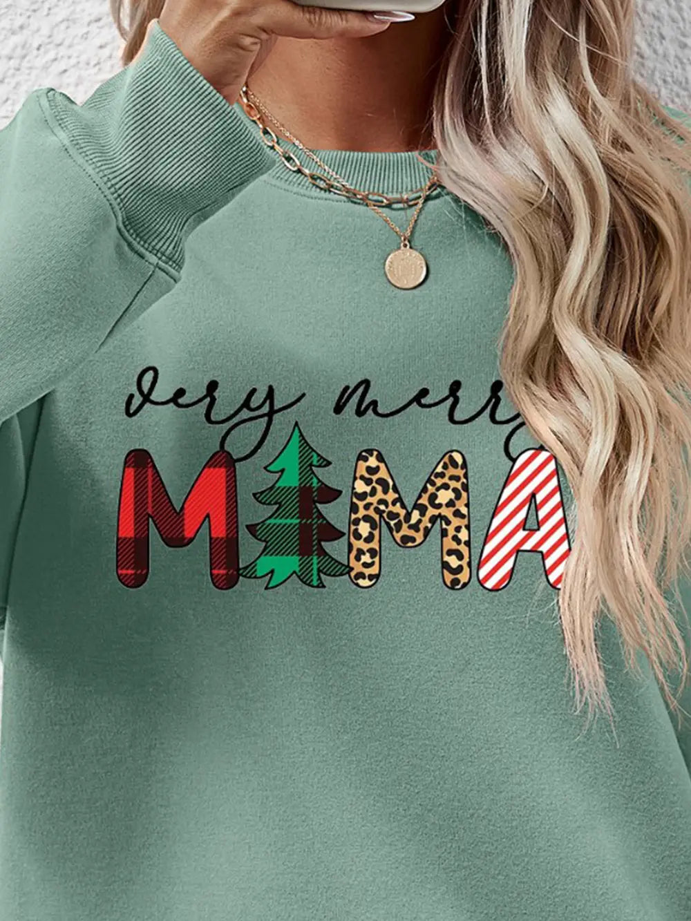Sage green crewneck sweater with "Very Merry Mama" graphic featuring plaid, tree, leopard print, and stripes.
