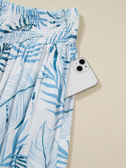 Tropical leaf print wide leg pants with smocked waist and side pocket holding a phone.