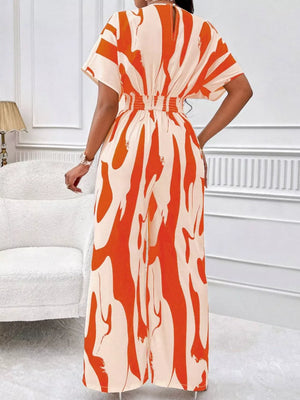 Chic abstract print wide-leg romper in orange and cream with short sleeves and elastic waist.