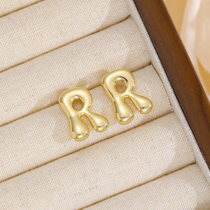 Alphabetical sculpted stud earrings in gold, featuring the letter R.