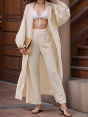 Voluminous sleeve duster and wide leg pants set in tan, styled with a white bikini top and straw clutch.