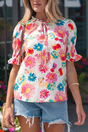 Women's white cotton blend shirt with vibrant floral print, tie neck, and ruched puff sleeves.