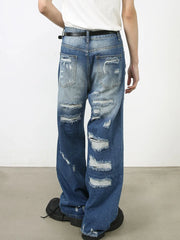 Oversized ripped denim jeans in medium wash with raw edge details and distressed accents.