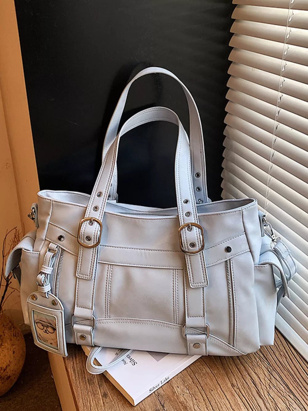 Light blue shoulder bag with buckle embellishments and multiple pockets.