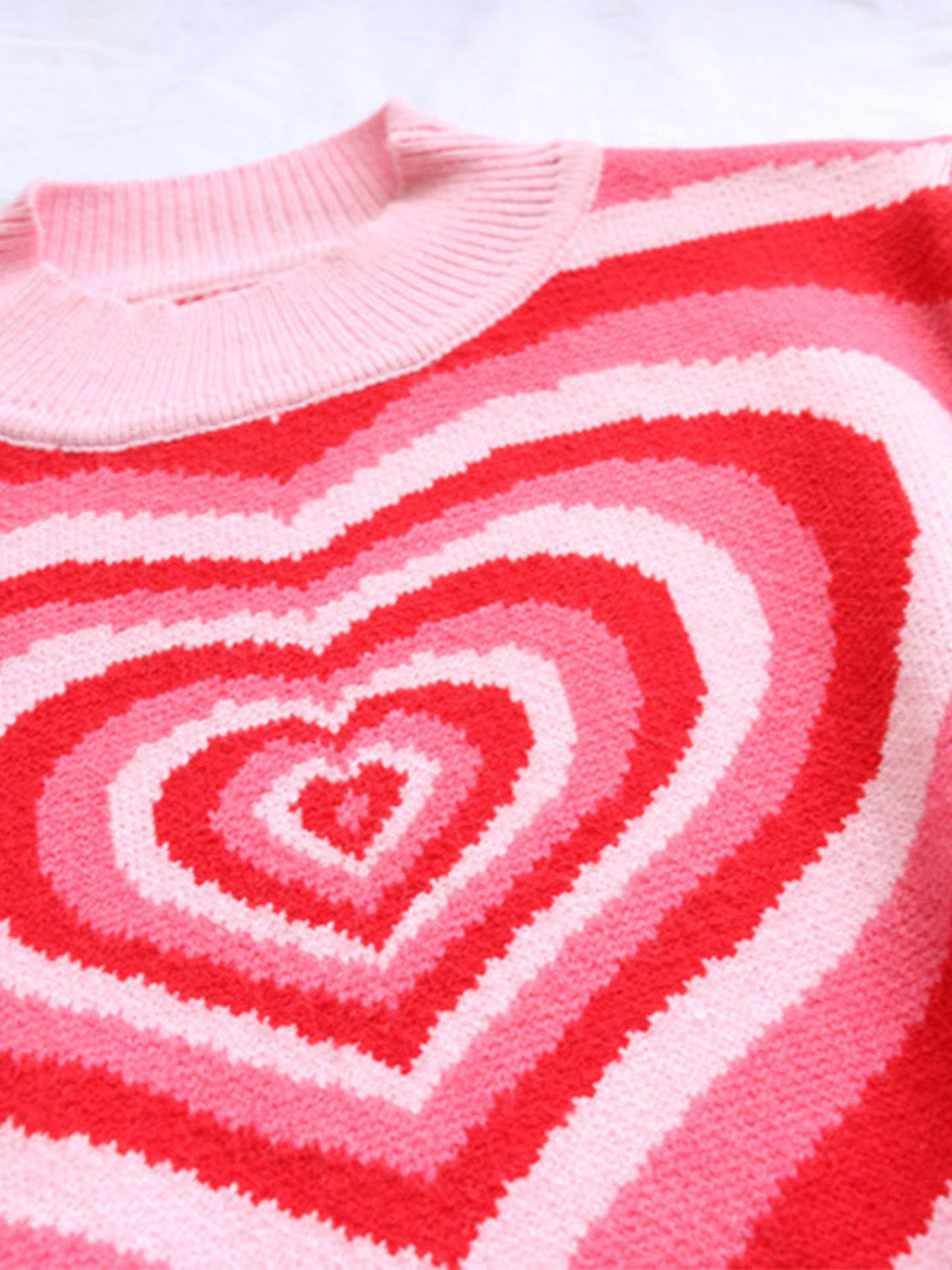 Mock neck knit sweater with concentric heart pattern in pink and red stripes.
