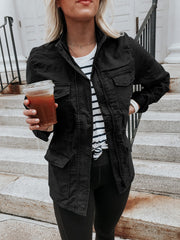 Black utility jacket with multiple pockets and a stand collar, worn over a striped tee.