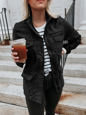 Black utility jacket with multiple pockets and a stand collar, worn over a striped tee.