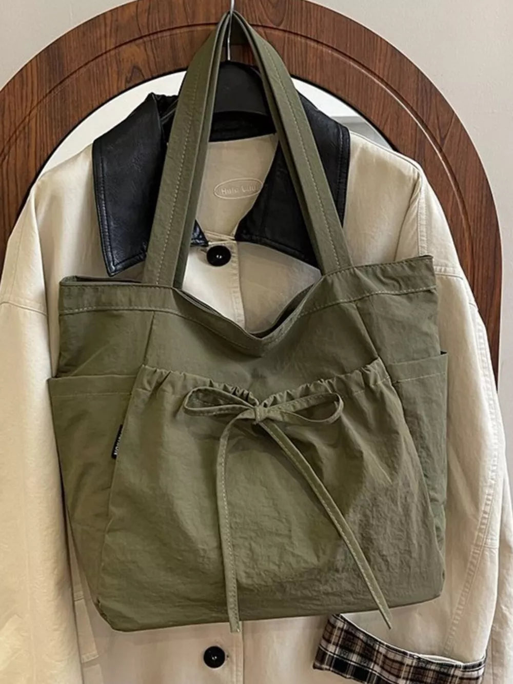 Olive green nylon tote bag with drawstring front pocket and bow detail.
