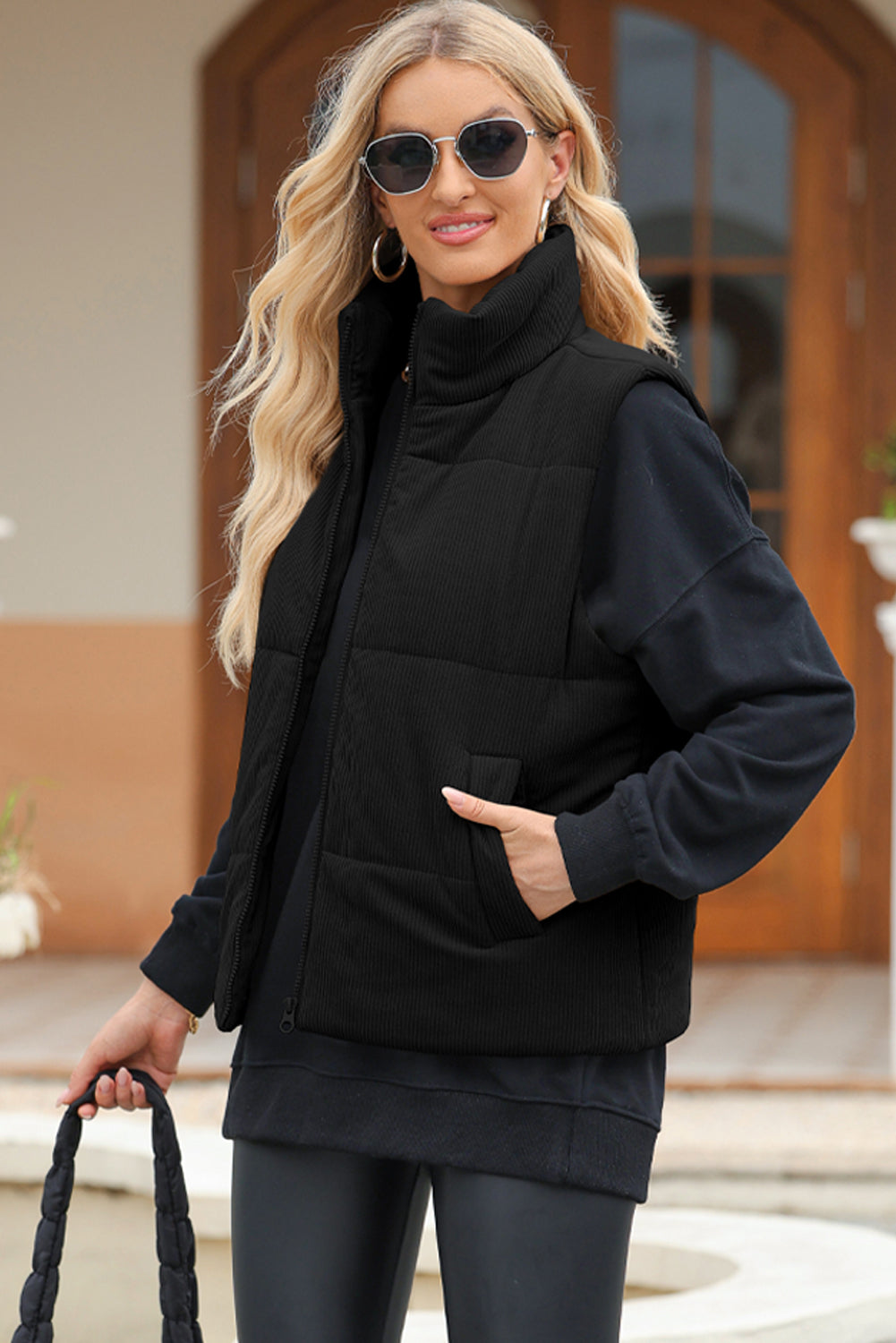 Black corduroy padded funnel neck vest with zip front and pockets, worn by a woman.