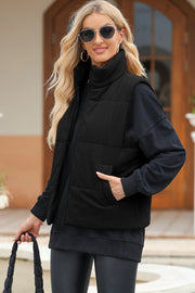 Black corduroy padded funnel neck vest with zip front and pockets, worn by a woman.