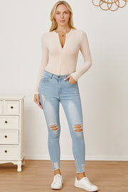 Ribbed long sleeve bodysuit in tan with plunge zip neckline, styled with ripped jeans.