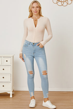 Ribbed long sleeve bodysuit in tan with plunge zip neckline, styled with ripped jeans.