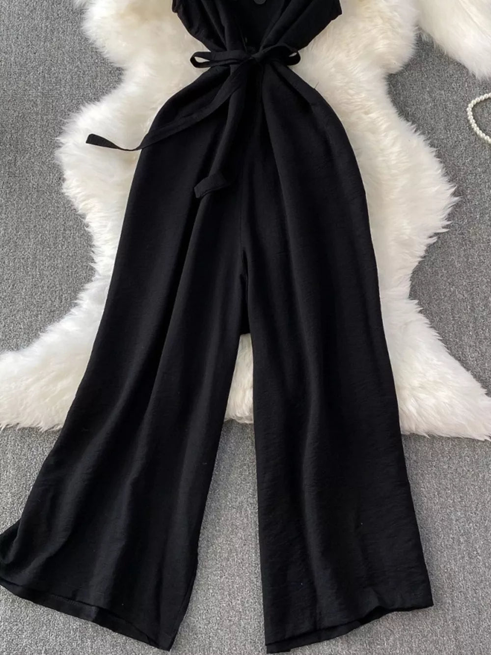 Black V-neck wide leg jumpsuit with belted waist and button details.
