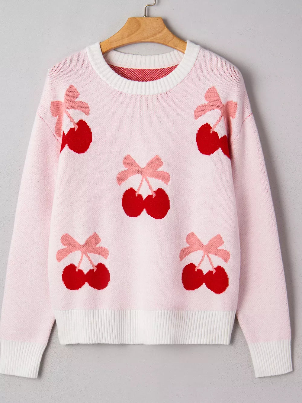 Pink knit sweater with all-over red cherry and pink bow appliqué pattern.