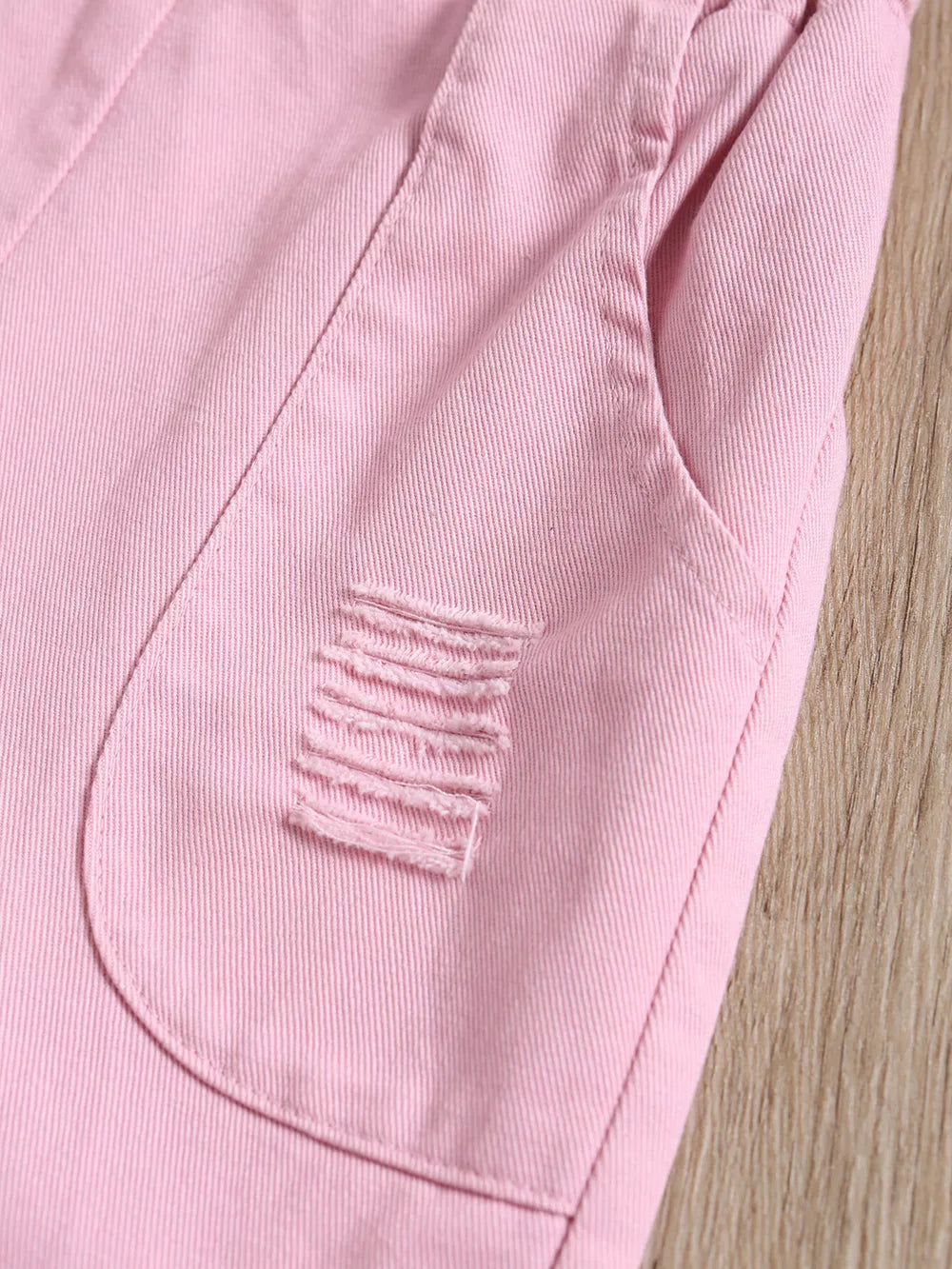 Pink distressed denim overalls for baby girls with frayed pocket detail.