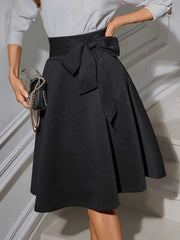 Black polyester midi skirt with a flared cut and a prominent bow-tie waist detail.