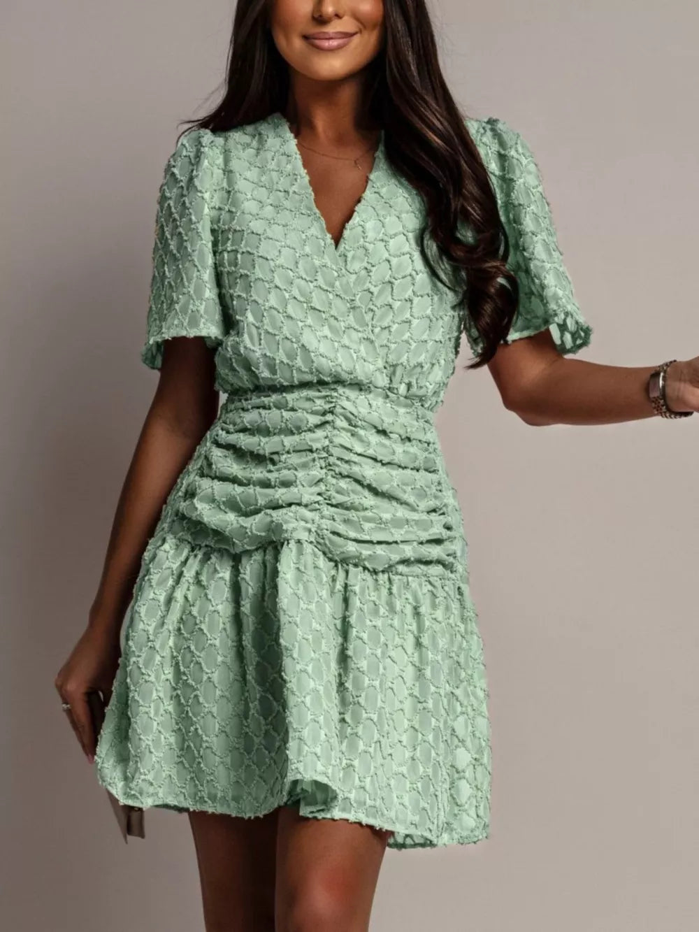 Textured light green ruched V-neck mini dress with short puff sleeves.