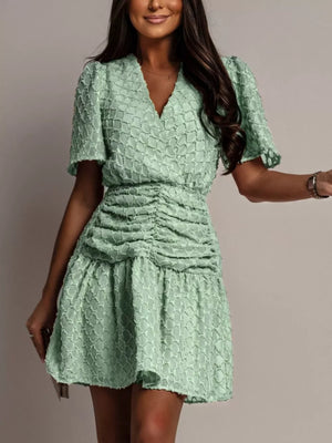 Textured light green ruched V-neck mini dress with short puff sleeves.