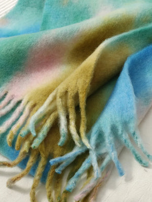 Watercolor wash fringe scarf in pastel blue, brown, and blush pink with soft, fuzzy texture.