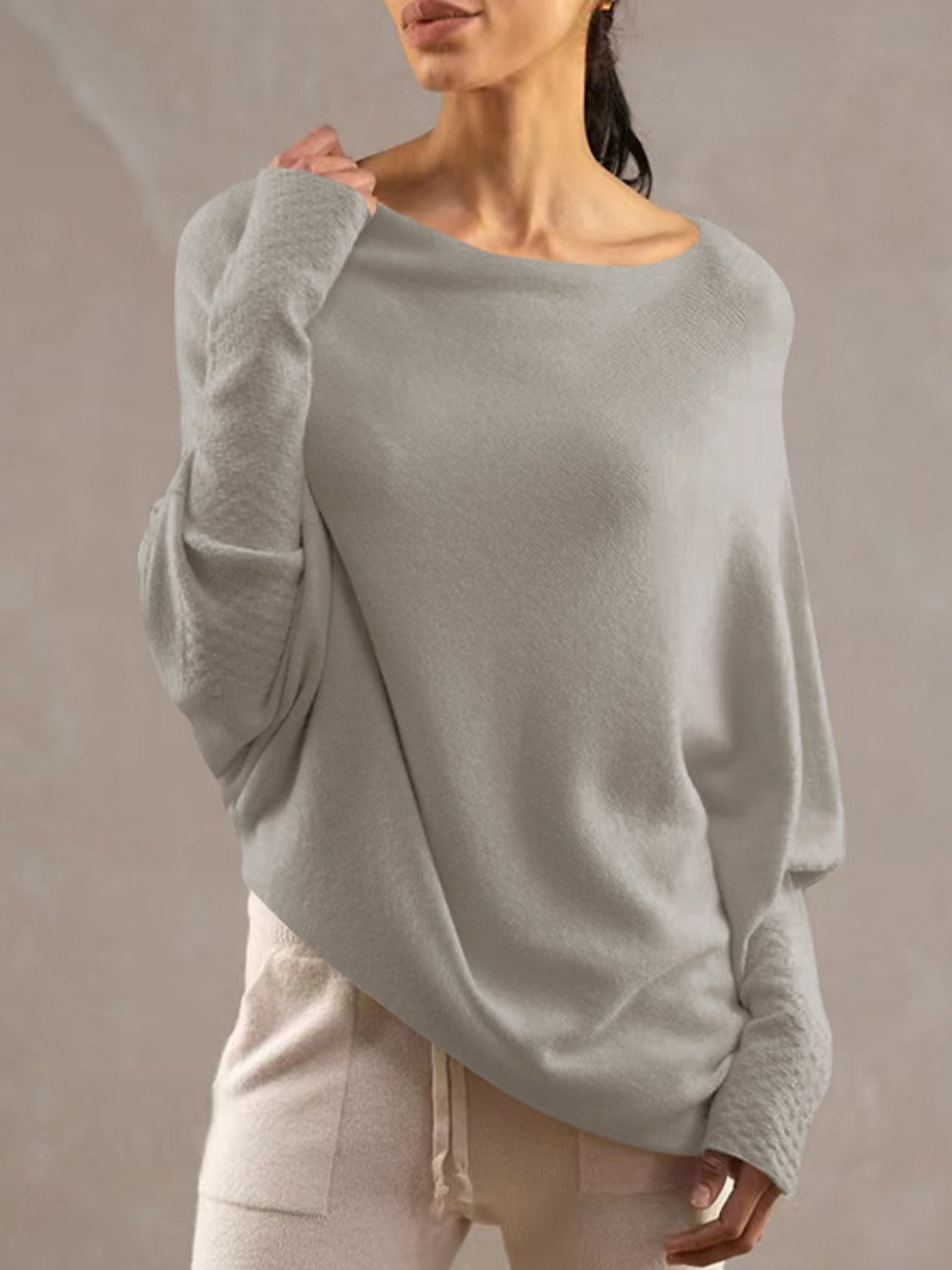 Light gray off-shoulder knit sweater with textured cuffs and draped fit.