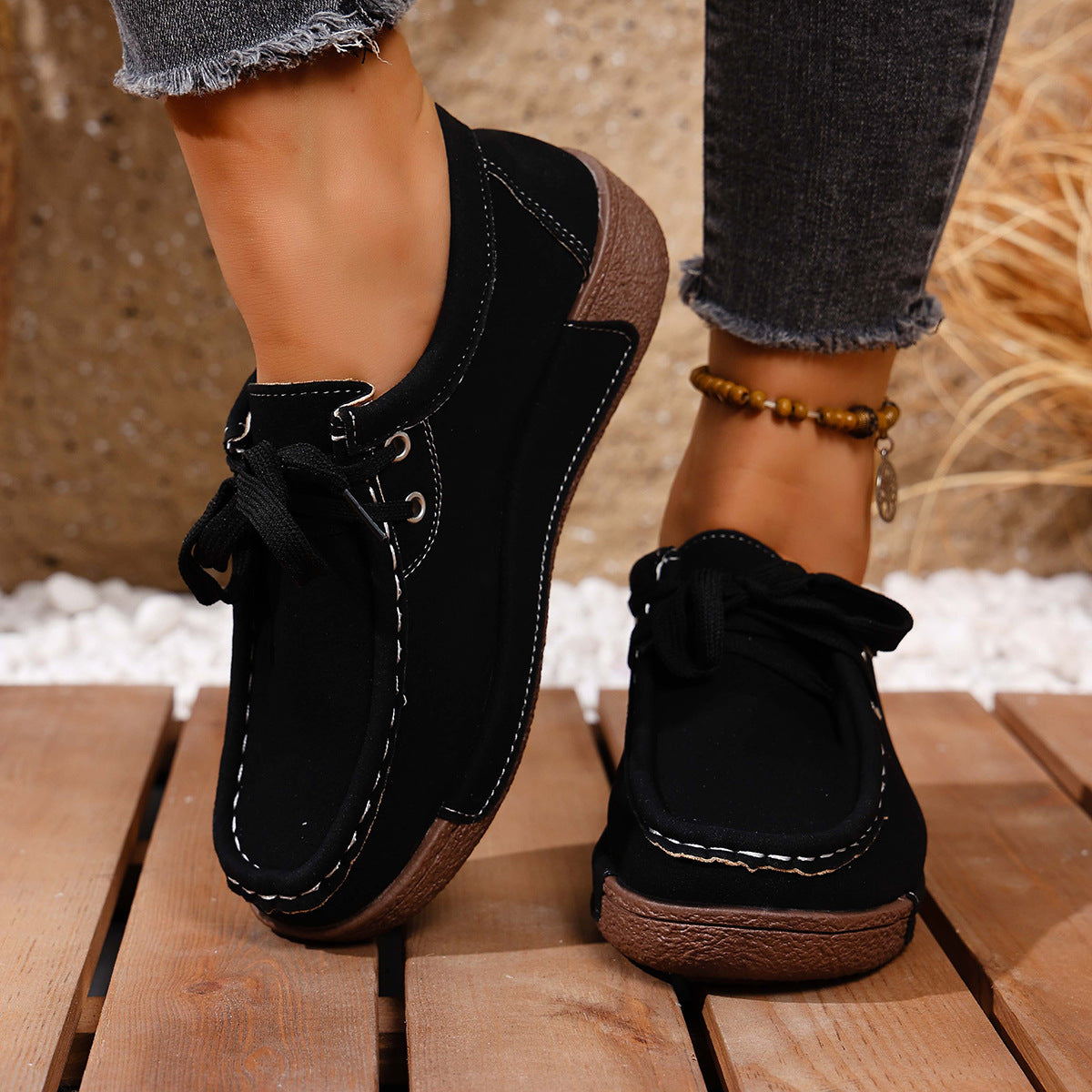 Black lace-up moccasin style sneakers with white contrast stitching and brown soles.