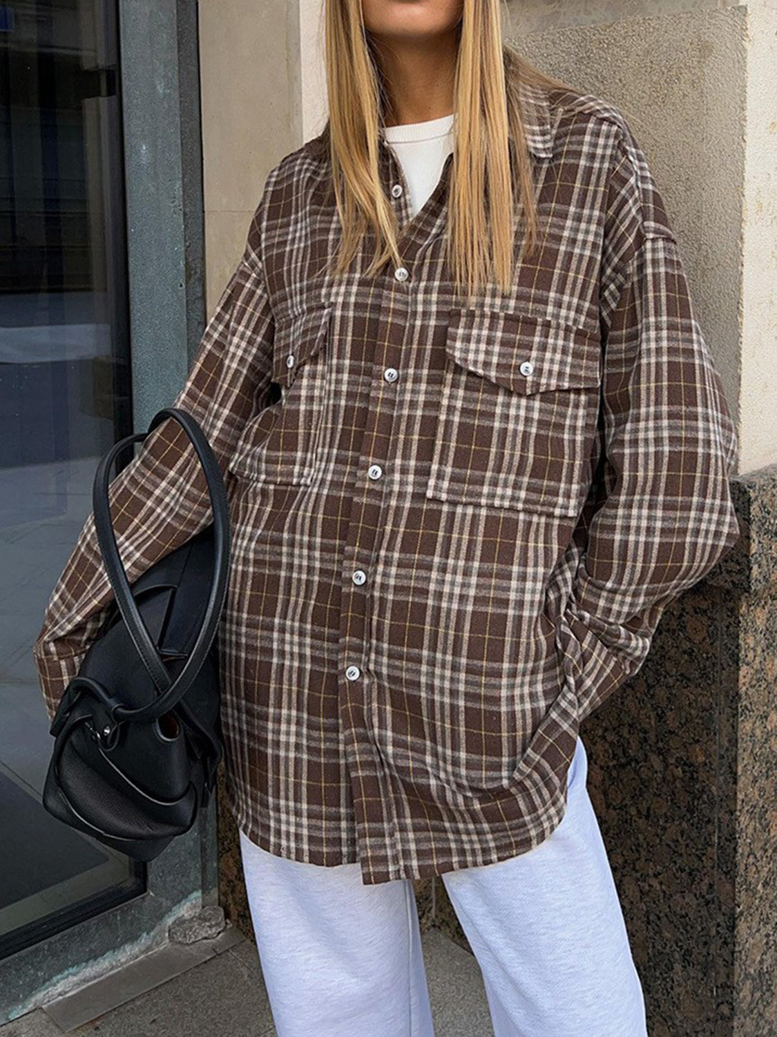 Brown plaid shacket with button-up front and chest pockets, worn open over a white tee.