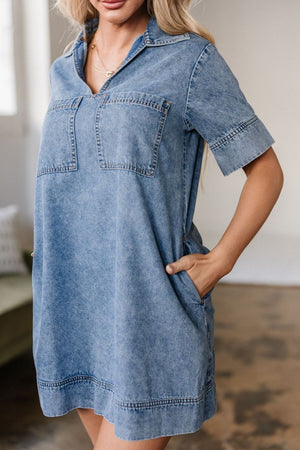 Light blue denim mini dress with short sleeves, collar, and two chest pockets.